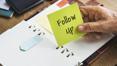 Close-up of a man's holding a sticky note that has the phrase 'follow up' written on it