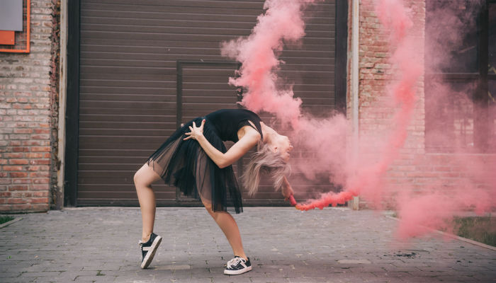 A young woman dancing in pink smoke on a street