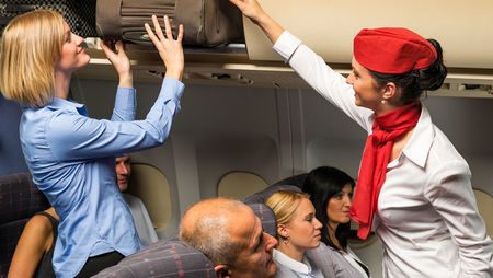 A female flight attendant helping a passenger with her luggage